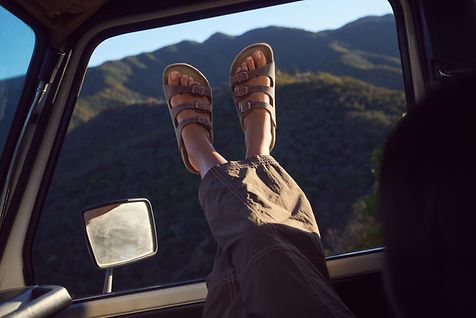 Frauenbein vor einem Autofenster in Sandalen