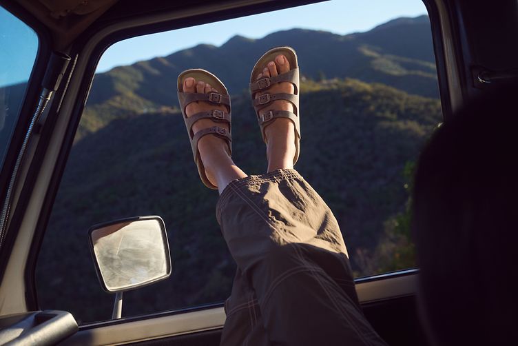 Frauenbein vor einem Autofenster in Sandalen